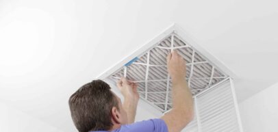 Caucasian male removing a square pleated dirty air filter with both hands from a ceiling air duct