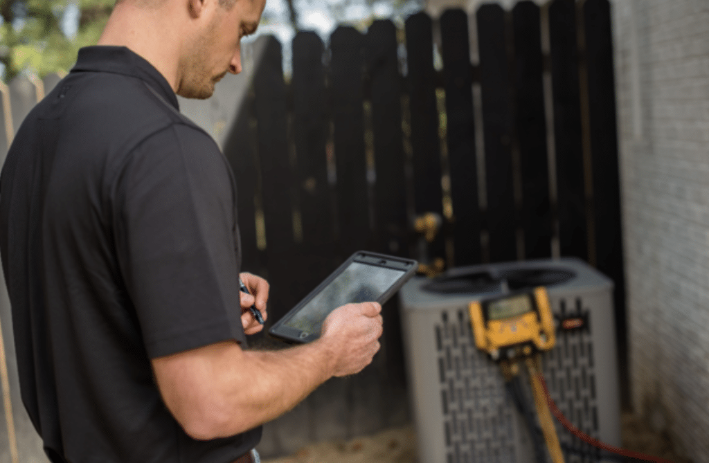 hvac technician looking at ipad while manometer performs air conditioning tune-up in the background